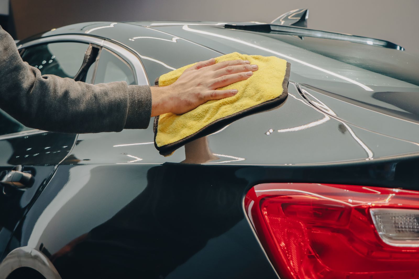 Hand polishing the rear panel of a dark car